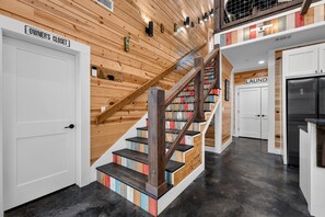 A staircase with wooden steps and a metal railing, leading to a laundry area with a stainless steel refrigerator.