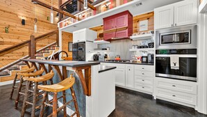 A modern kitchen with white cabinetry, a central island with stools, and a red accent wall. - Creek Bluff Retreat for Large Families and Groups (Broken Bow)