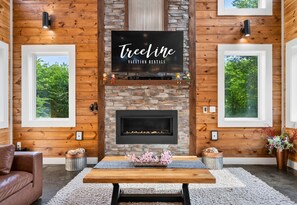 A cozy room with a fireplace, a TV mounted on the wall, and a sign for TreeLine Vacation Rentals.