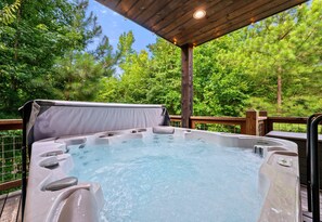 Un bain à remous sur une terrasse extérieure, avec un plafond en bois et entouré d’arbres.