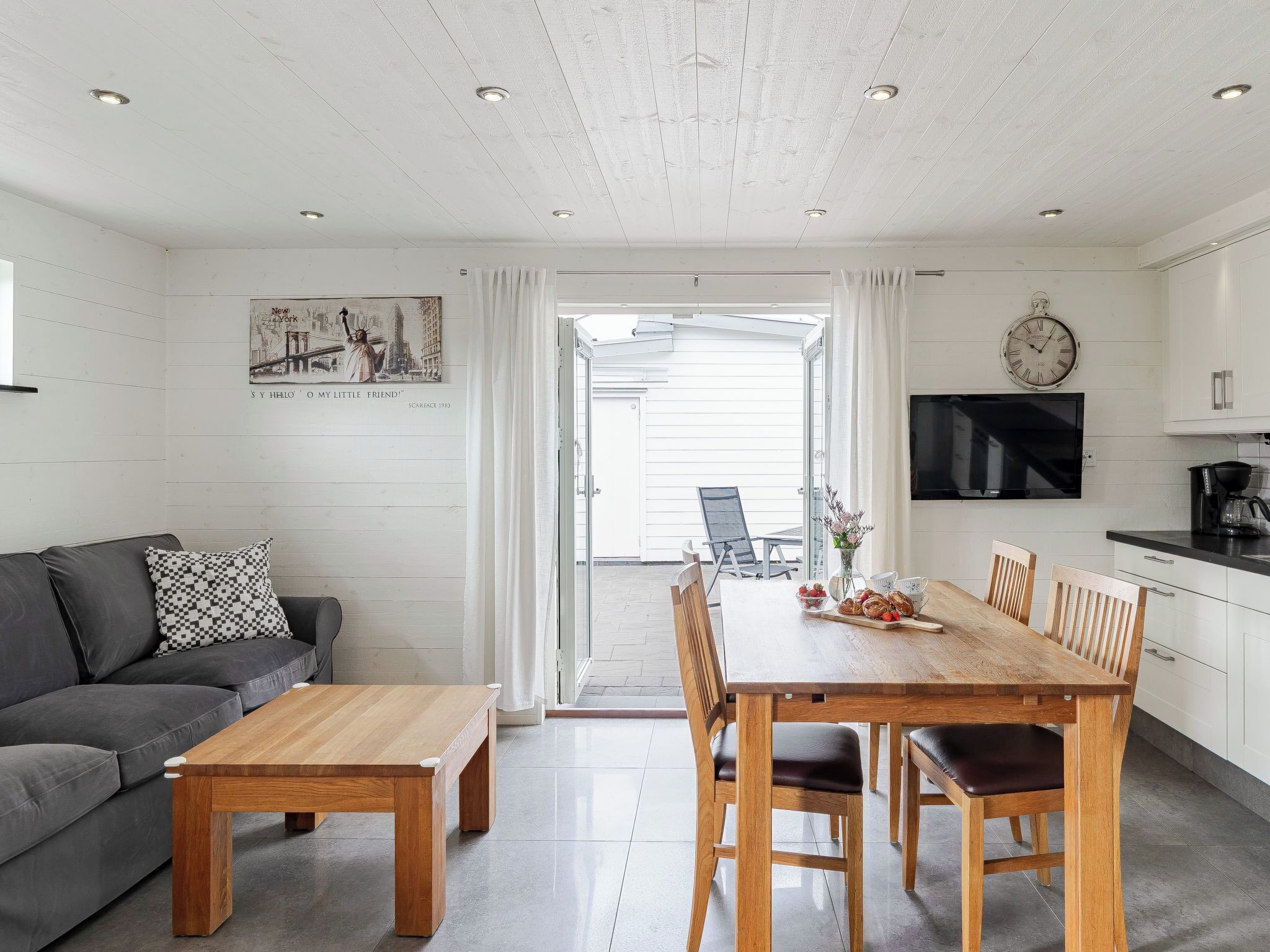 A modern kitchen with white cabinets, a wooden dining table, and a black TV.