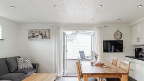 A modern kitchen with white cabinets, a wooden dining table, and a gray sofa. - Östra Stranden by Interhome (Halmstad)