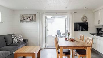 A modern kitchen with white cabinets, a wooden dining table, and a black TV.