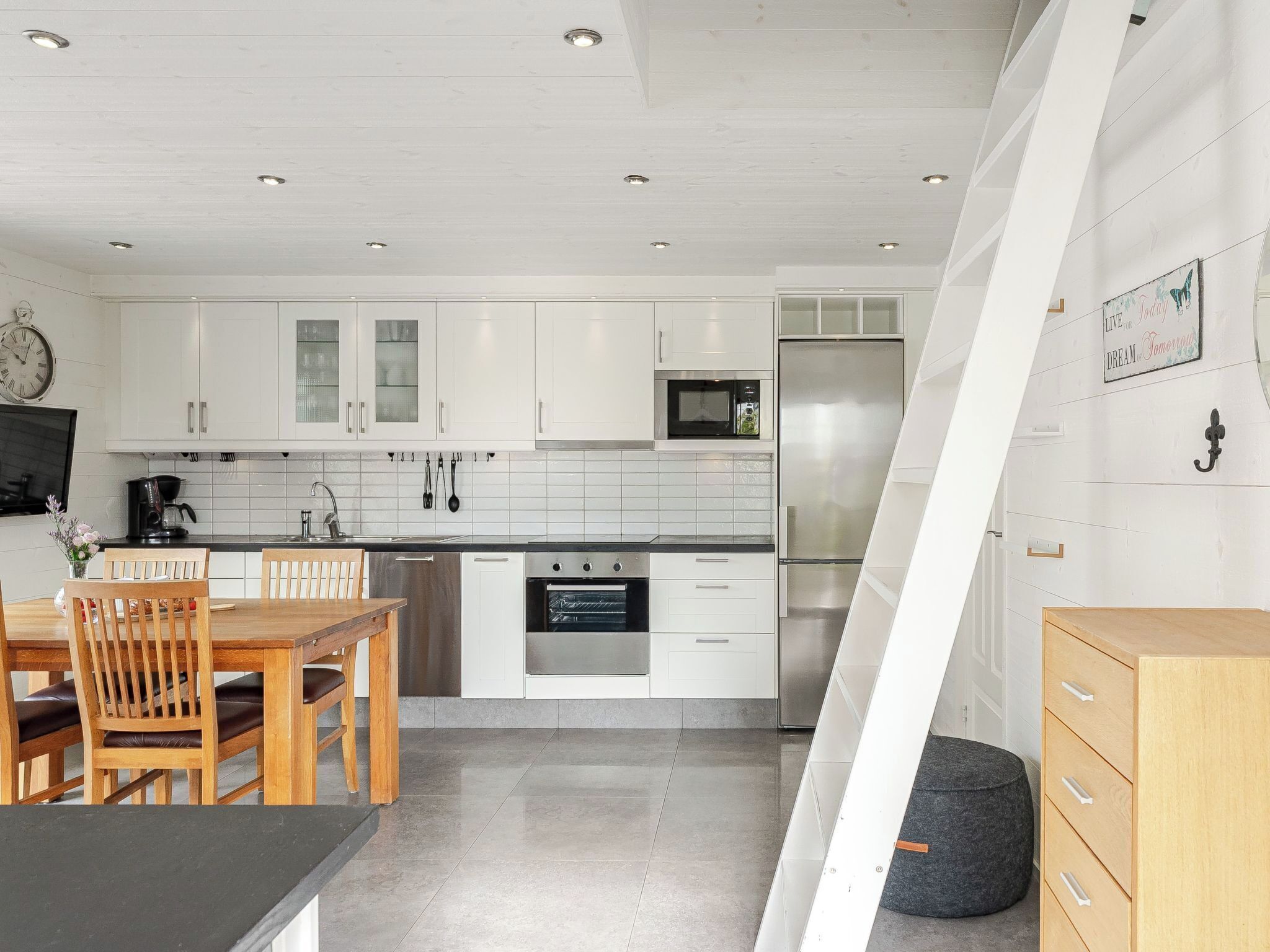 A modern kitchen with white cabinets, stainless steel appliances, and a dining area with wooden furniture.