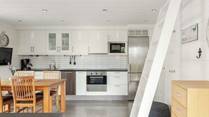 A modern kitchen with white cabinets, stainless steel appliances, and a dining area with wooden furniture. - Östra Stranden by Interhome (Halmstad)