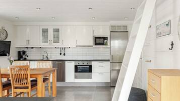 A modern kitchen with white cabinets, stainless steel appliances, and a dining area with wooden furniture.
