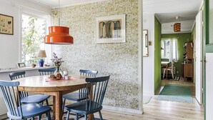 Un comedor con mesa de madera, sillas azules y una lámpara colgante roja. Se observa papel tapiz con diseño y un cuadro en la pared.