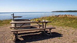 Una mesa de picnic con una parrilla y un juego de tazas sobre una zona de grava junto al agua.