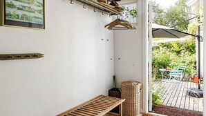 Una habitación con un banco de madera, una cesta de mimbre, un perchero metálico con sombreros y un cuadro en la pared.
