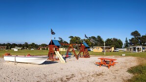Una playa con un parque infantil, una mesa de picnic y un bote.