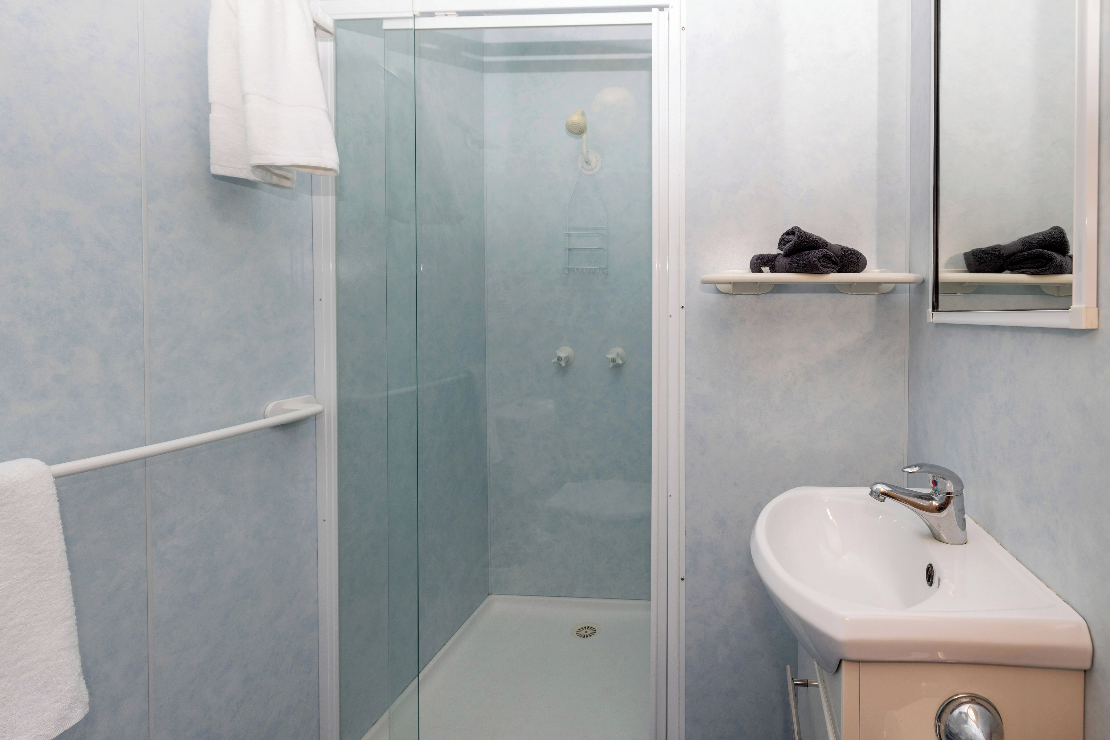Un baño con ducha envuelta en vidrio, un lavamanos blanco y un perchero para toallas.