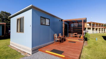 Een laag, enkel verhaal tellend gebouw met een blauwe gevel, een houten terras en een overdekt zitgedeelte met tafels en stoelen.
