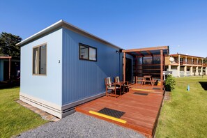 Un petit bâtiment d’un seul étage, à l’extérieur bleu, doté d’une terrasse en bois et d’un espace extérieur abrité avec des tables et des chaises.
