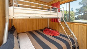 Un lit superposé avec vue sur la fenêtre, des murs en bois et une serviette rouge.