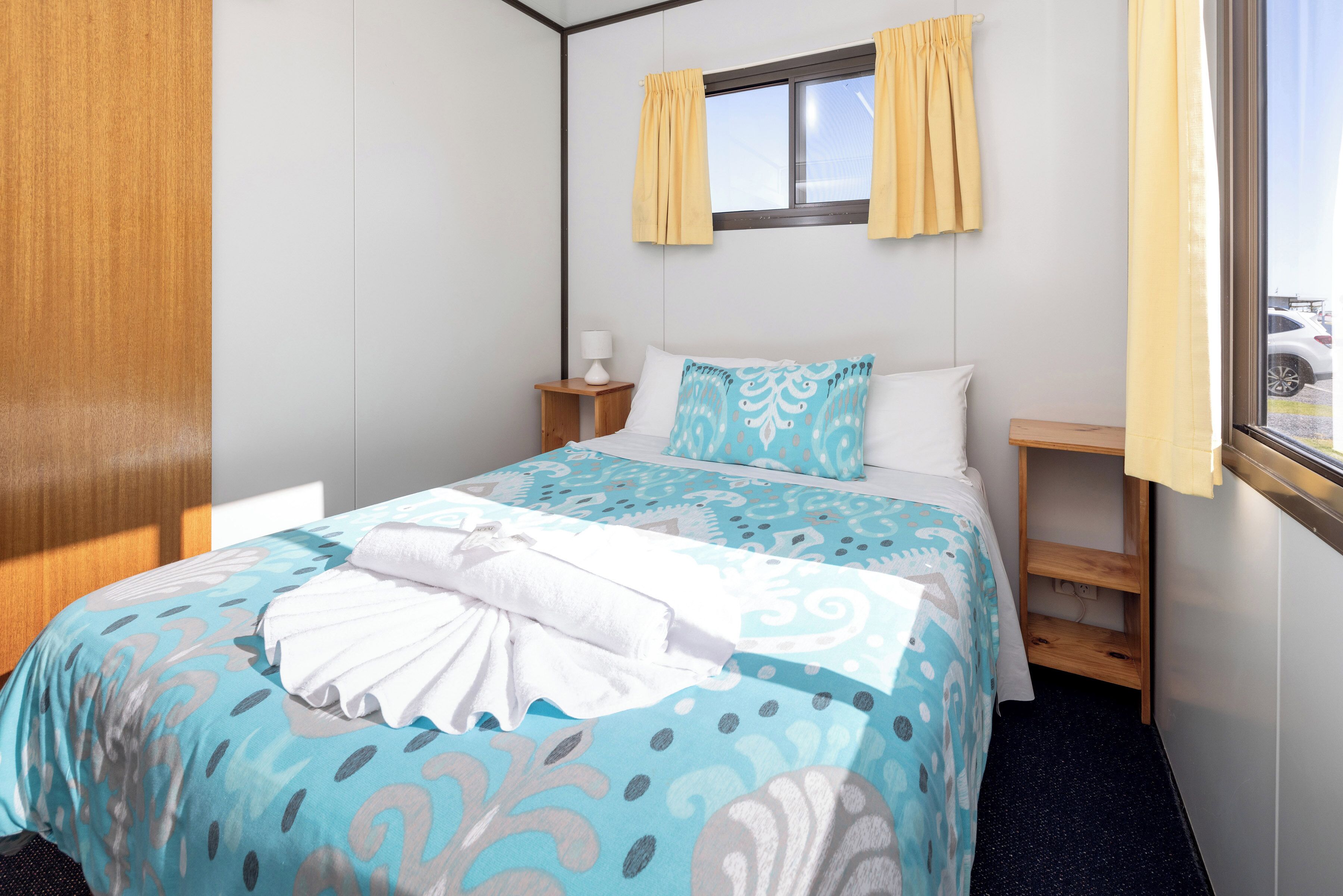 Une chambre d’hôtel avec un lit, une table de chevet, une fenêtre avec des rideaux et une vue sur l’extérieur.