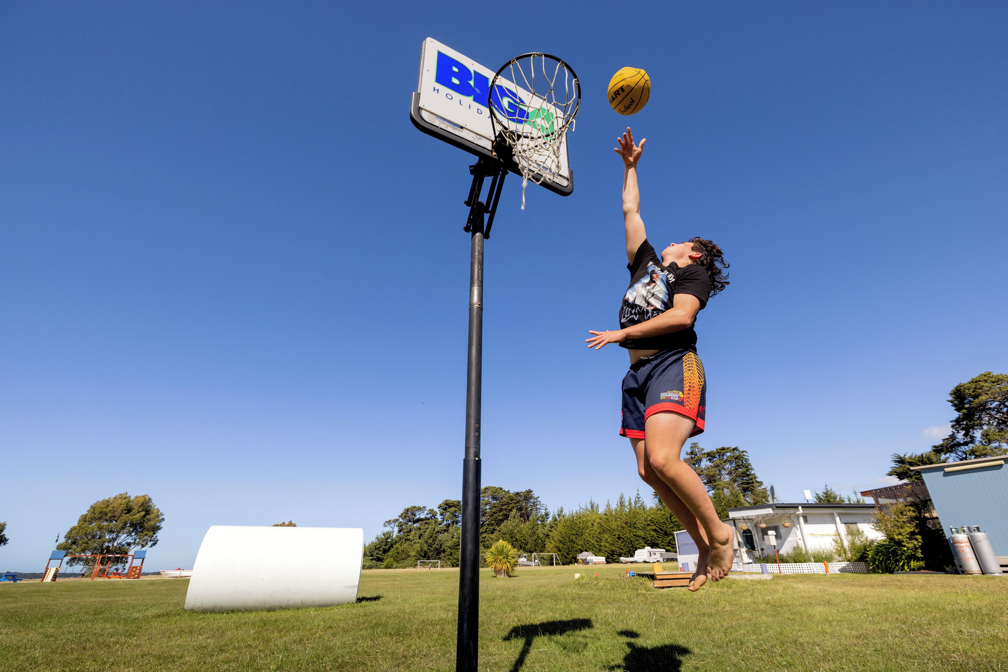 A basketball hoop with a net, a clear blue sky, and a grassy field.