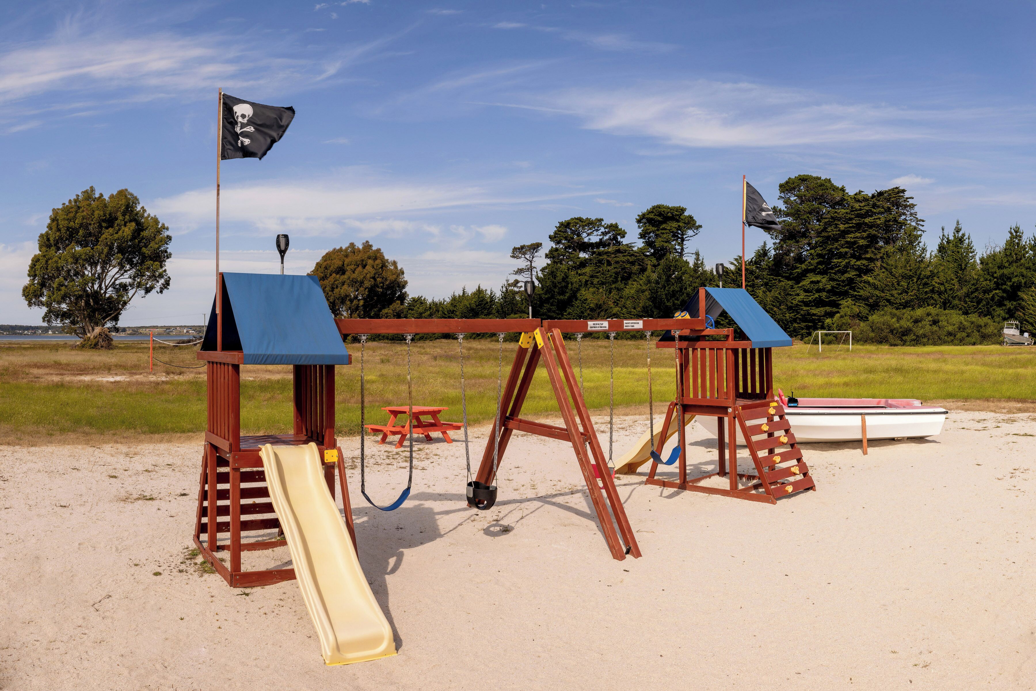 A beach playground with a slide, swings, and a small boat.
