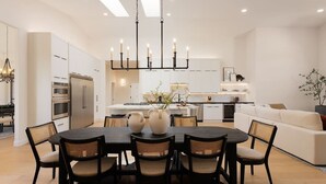A modern kitchen with a central island, dining table with chairs, and a chandelier.