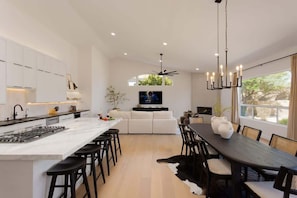 Una cocina moderna con una isla central, un comedor con mesa de madera oscura y una sala de estar con sofá y televisor.