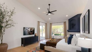 A modern bedroom with a bed, a ceiling fan, a TV, a potted plant, and a large window.