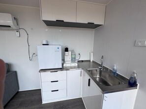 Una cucina compatta con frigorifero integrato, macchina del caffè e dispenser per l'acqua.