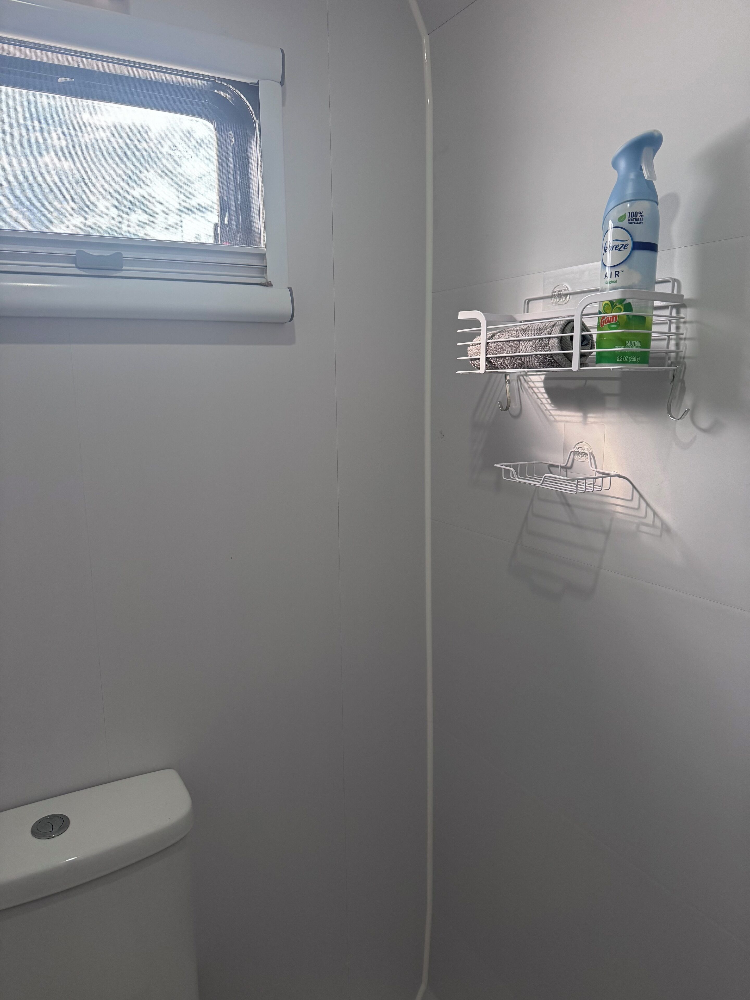 Ein Badezimmer mit Toilette, Fenster und Ablage für Reinigungsmittel.