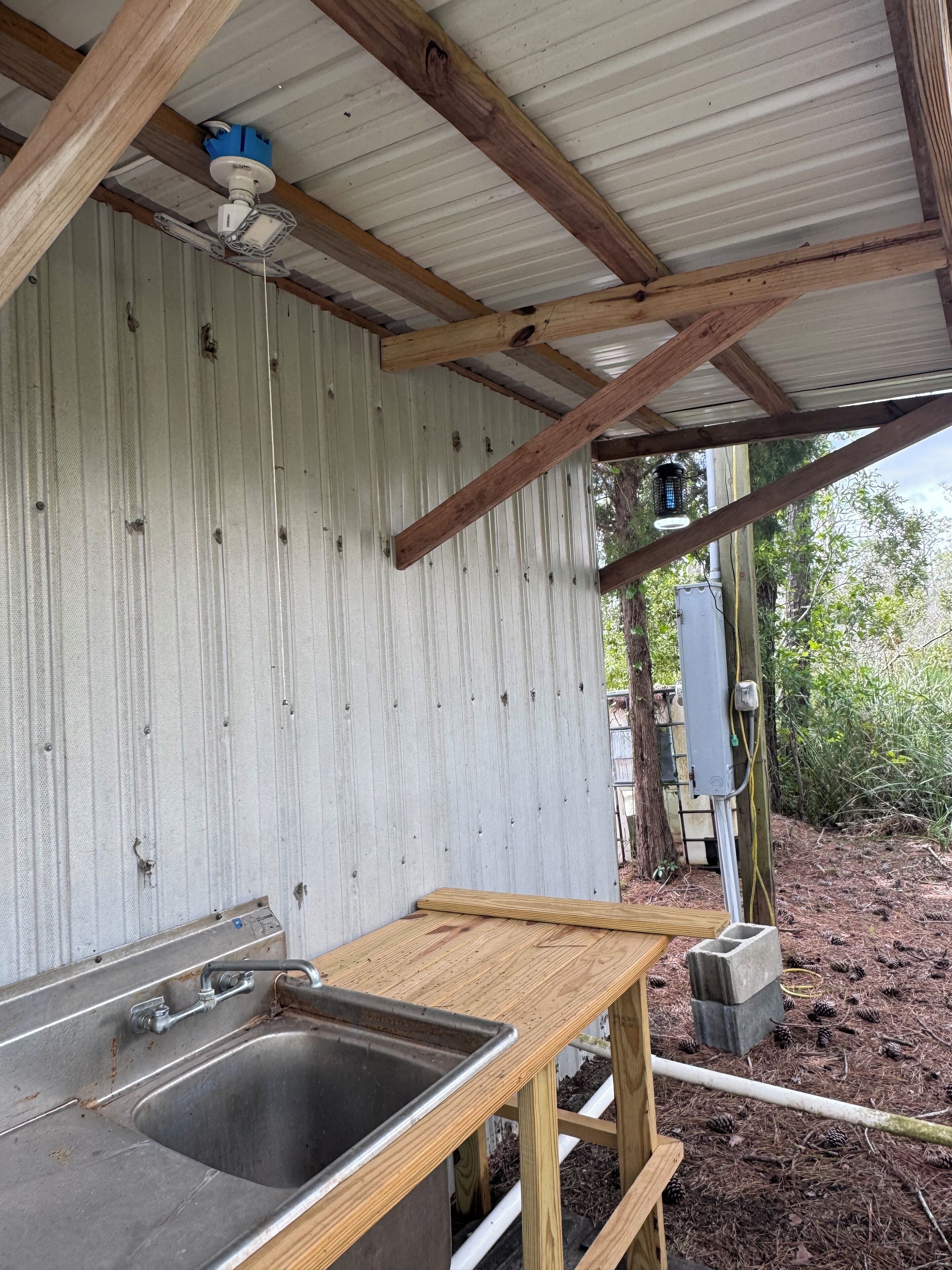 Eine rustikale Außenküche mit Spüle aus Metall, Holztisch und Deckenventilator.