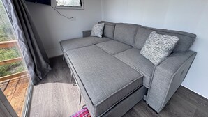 Et moderne, kompakt værelse med en grå sofa, et lille vindue og udsigt til grønne områder.