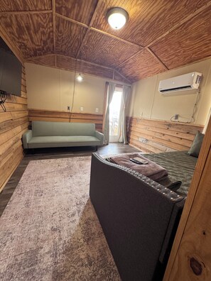 Un interno accogliente di una baita con un divano, un letto, un tavolino e un condizionatore d'aria.