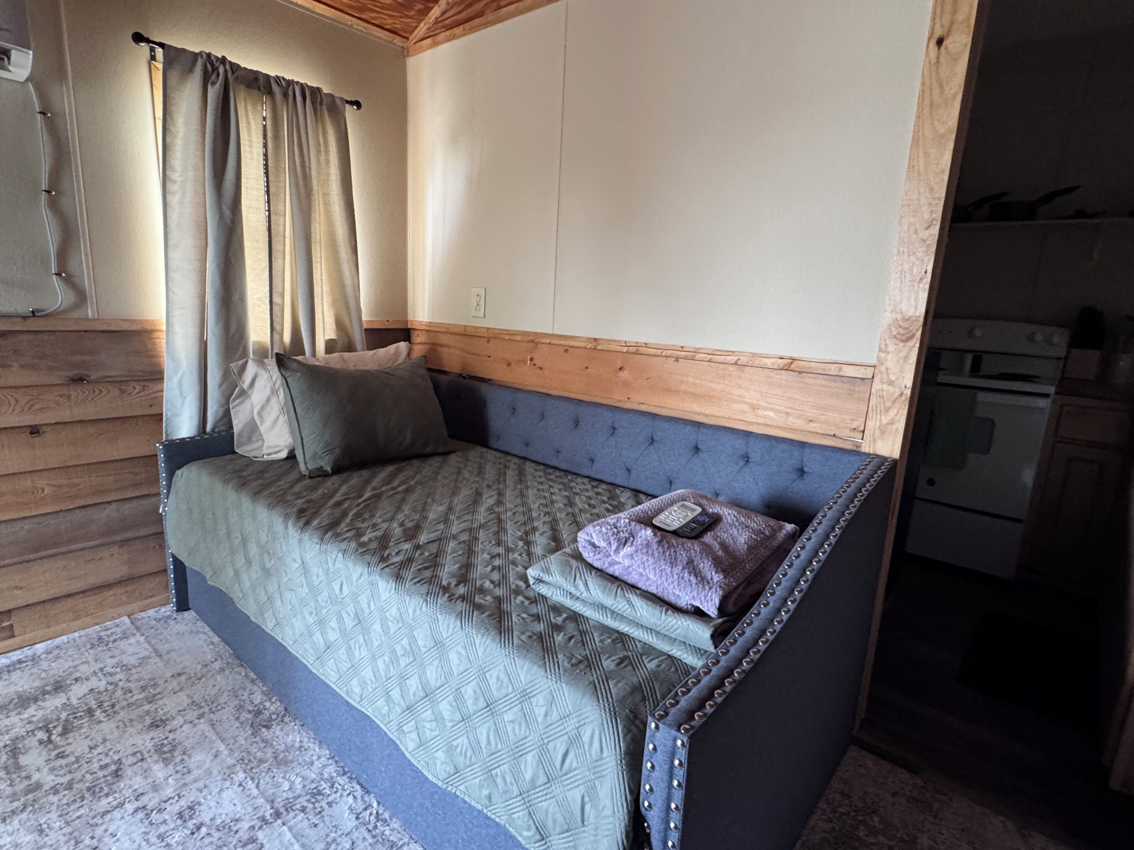 A cozy room with a bed, wooden headboard, and a kitchenette.