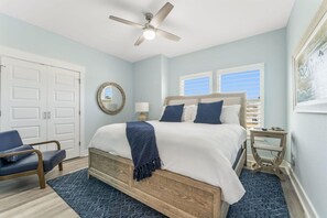 A bedroom with a bed, a ceiling fan, a chair, a nightstand, and a window with blinds.