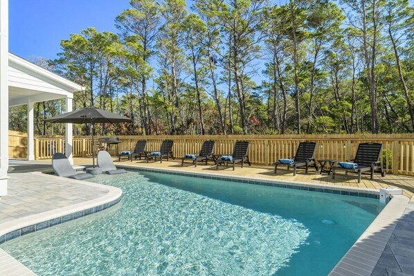 A swimming pool with lounge chairs and a covered area, surrounded by trees.
