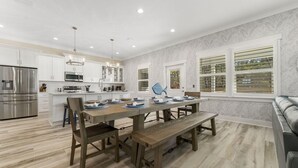 Una cocina moderna con armarios blancos, electrodomésticos de acero inoxidable y un comedor con una mesa de madera y bancos.