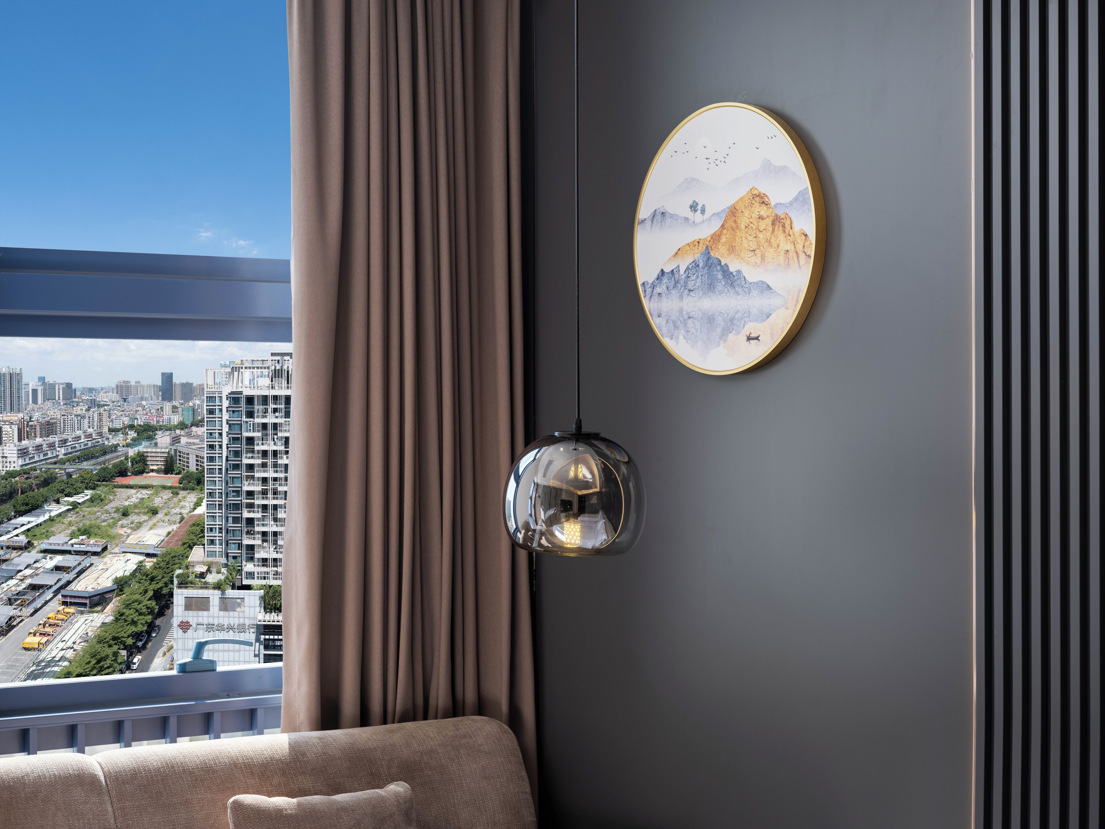 A modern living room with a city view, a round mirror, and a framed artwork on the wall.