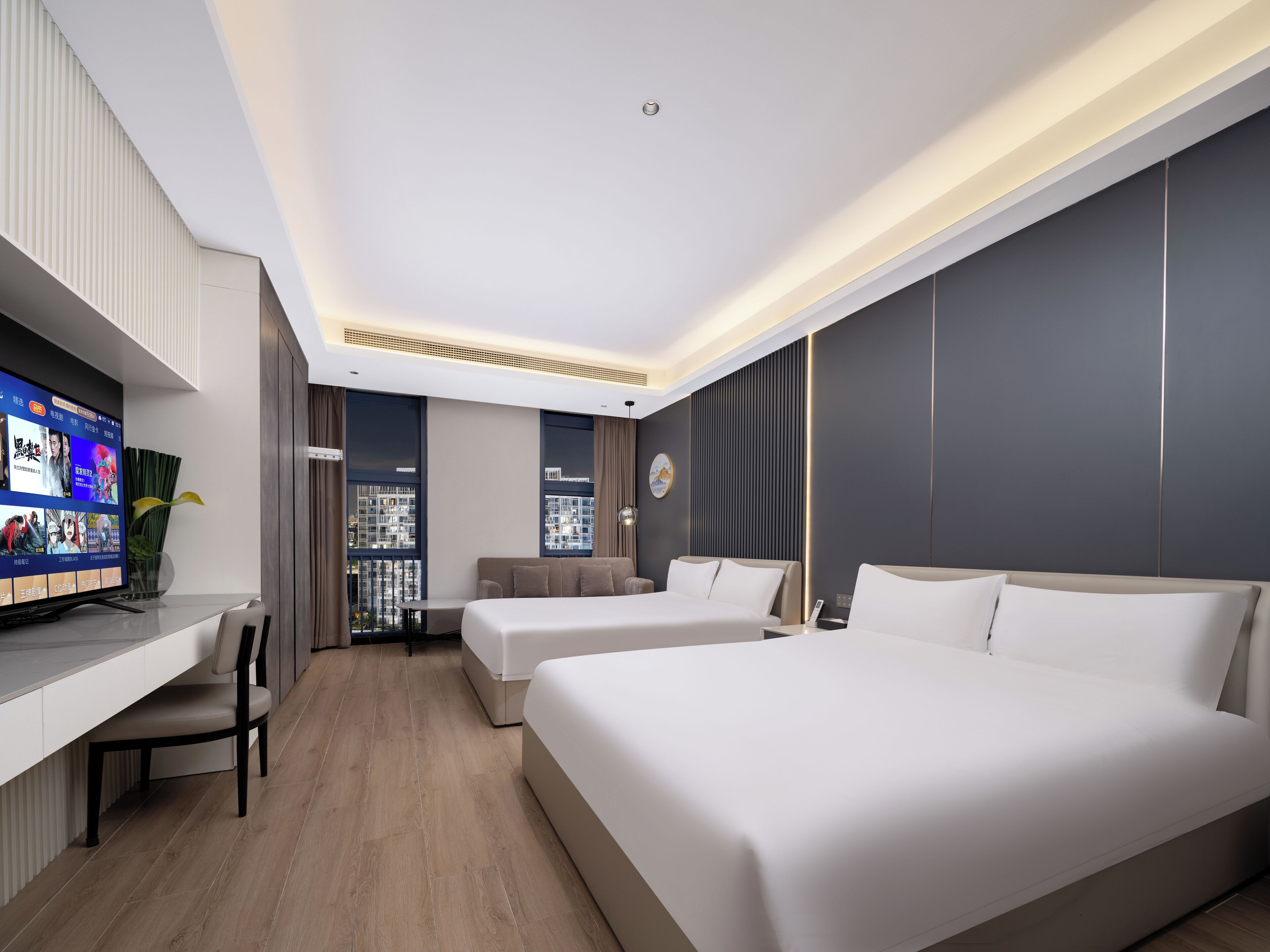 A modern hotel room with two beds, a desk, and a TV displaying a movie.