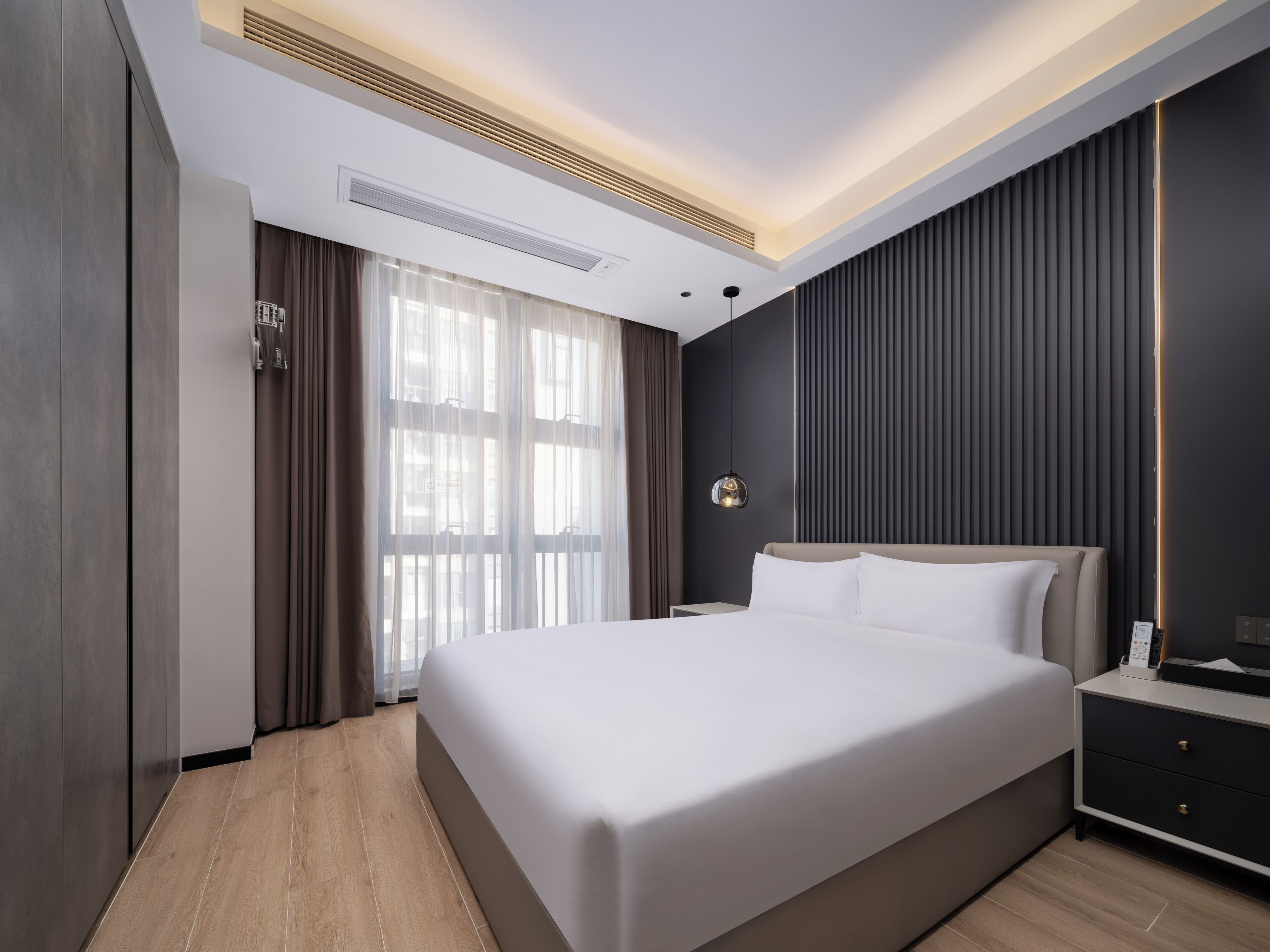 Ein modernes Hotelzimmer mit einem großen Bett, einem Nachttisch, einer Wandlampe und einem Fenster mit Vorhängen.