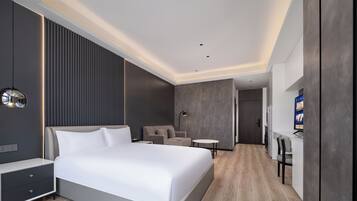 A modern hotel room with a large bed, a desk, a chair, and a TV.