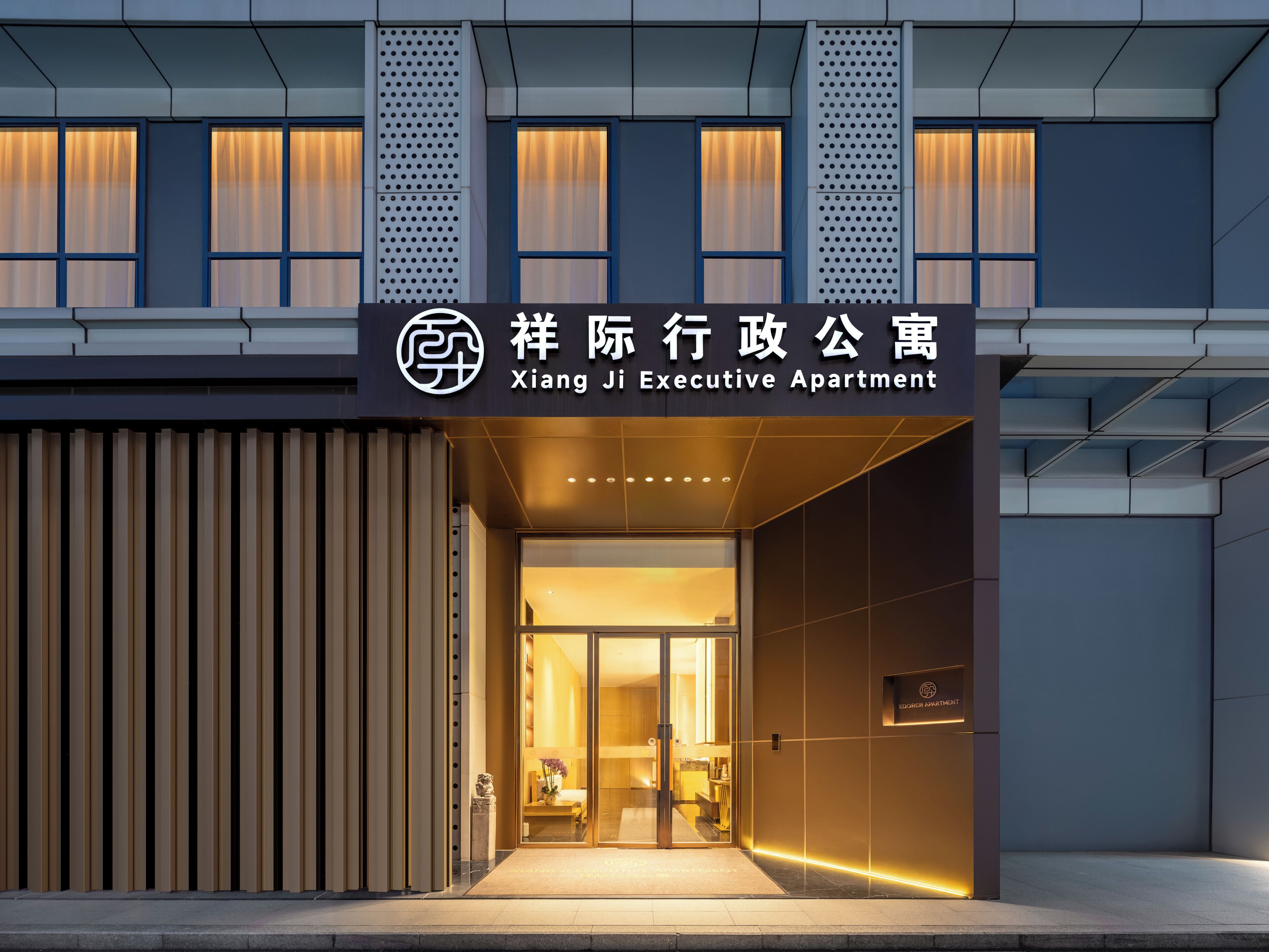 An entrance to Xiang Ji Executive Apartment with a modern design, featuring a glass door entrance and a signboard above.
