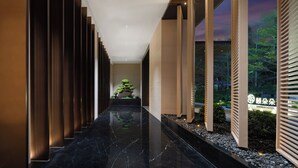Un pasillo moderno de hotel con piso de mármol negro reflectante, paneles de madera verticales y un cartel con el nombre del hotel.
