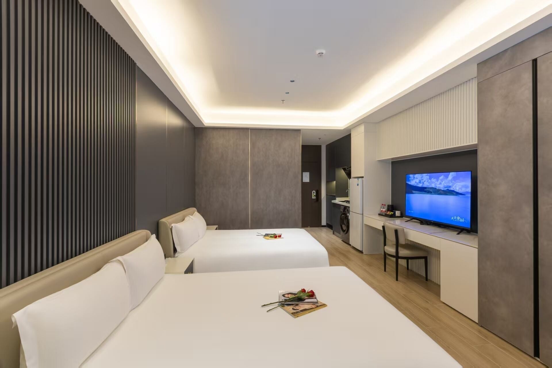 Una habitación de hotel moderna con dos camas, una kitchenette y un televisor.