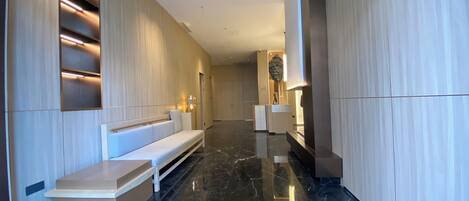 Un pasillo moderno de hotel con suelo de mármol, un sofá blanco y un mostrador de recepción.