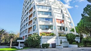 Un immeuble moderne à plusieurs étages, doté de balcons, d’un parking et entouré de verdure.