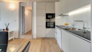 Una cocina moderna con armarios blancos, encimera negra, electrodomésticos de acero inoxidable y una mesa de comedor de vidrio.