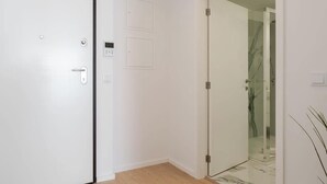 Un pasillo con una puerta blanca, una puerta de cristal que da a un baño y una planta pequeña a la derecha.