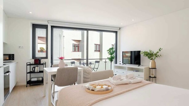 Una habitación de hotel moderna con una cama grande, un escritorio, un televisor y un balcón con vistas a edificios.