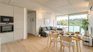 Una cocina moderna con electrodomésticos integrados, un comedor con sillas de madera y un amplio ventanal con vistas a la vegetación.
