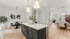 Una cocina amplia con isla central, iluminación colgante y un comedor con mesa y sillas.