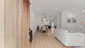 Ett rymligt vardagsrum med modern design, med en soffa i ljusa färger, trägolv och en matplats med bord och stolar.