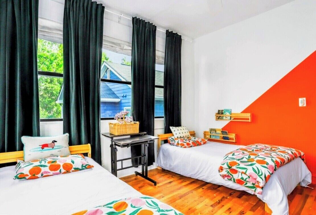 A room with two beds, a small table, and a window with curtains.