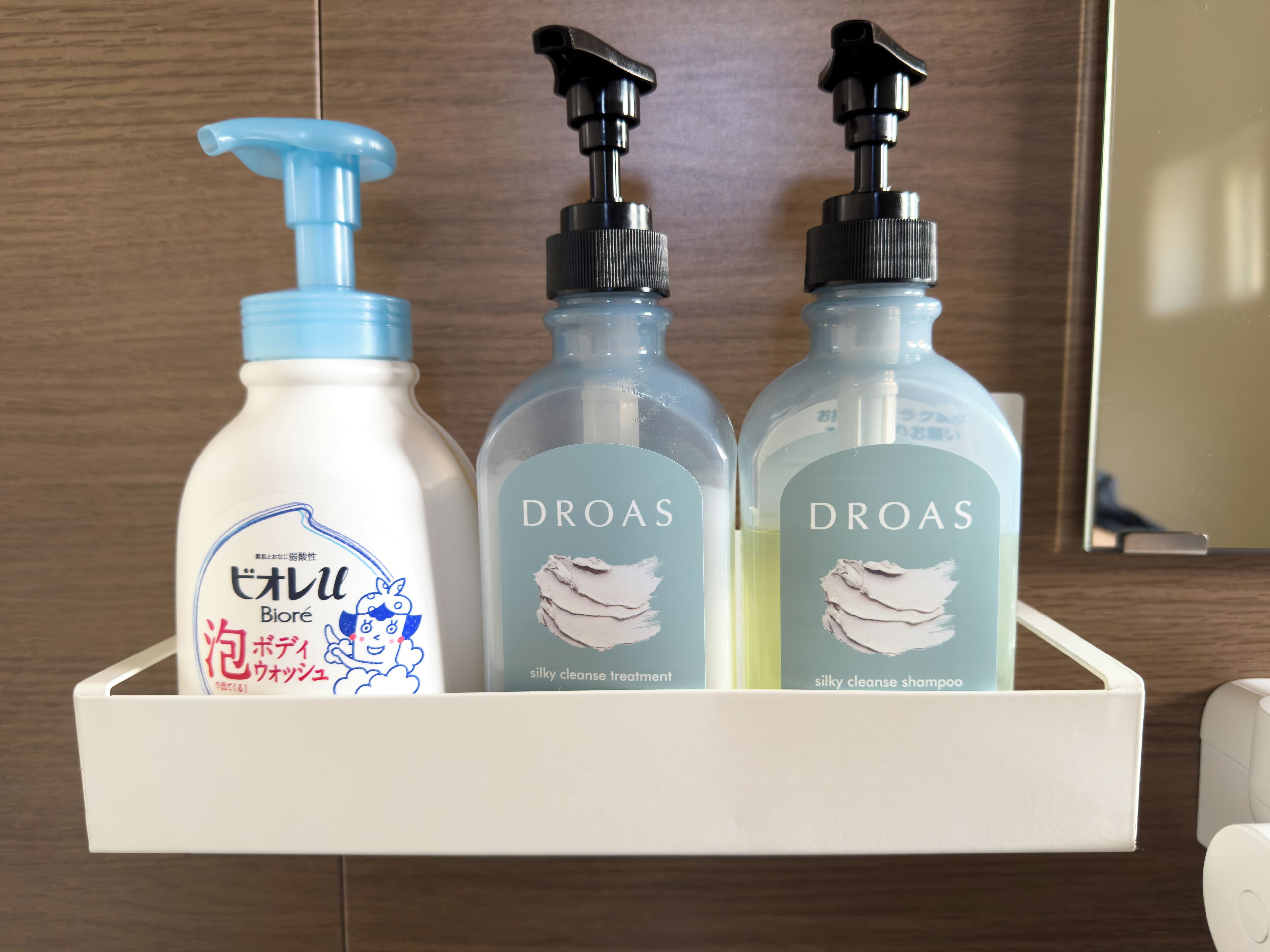 Trois flacons du traitement et du shampooing DRAAS, à la texture soyeuse, sont posés sur une étagère blanche.